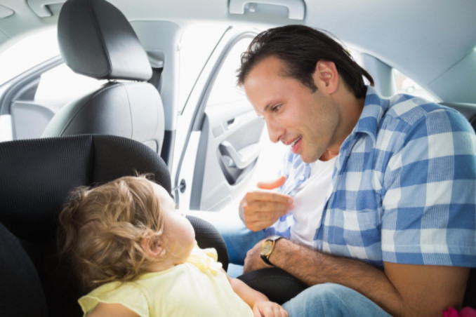 Man buckling child into car seat: WorkingManLaw.com Car Accident Blog