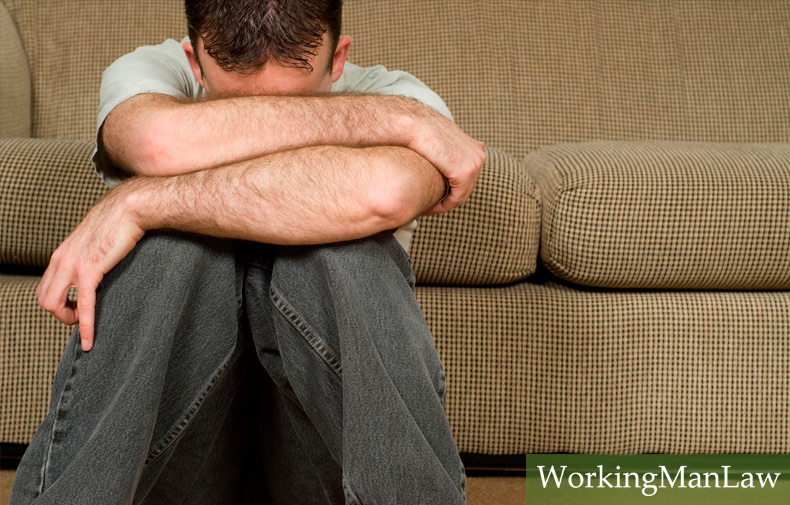 man suffering from depression sits on floor in front of couch with his head laying in his arms