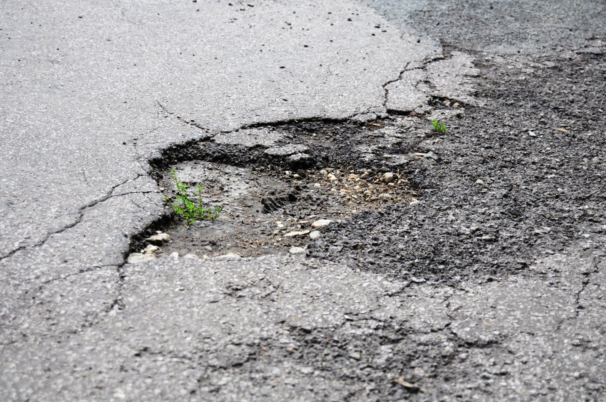 damaged car of road full of cracked potholes in pavement